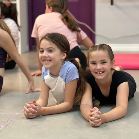 Girls smiling laying on their stomachs during warm up in dance class.